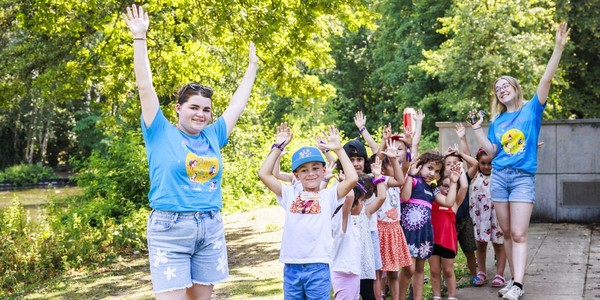 Twee animatoren en een groep kinderen houden allemaal hun armen omhoog.